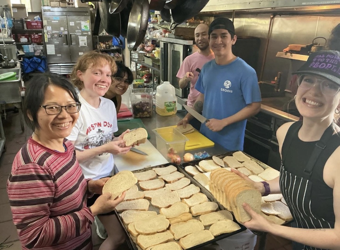 Volunteers slicing and laying out bread on sheet trays in a community kitchen