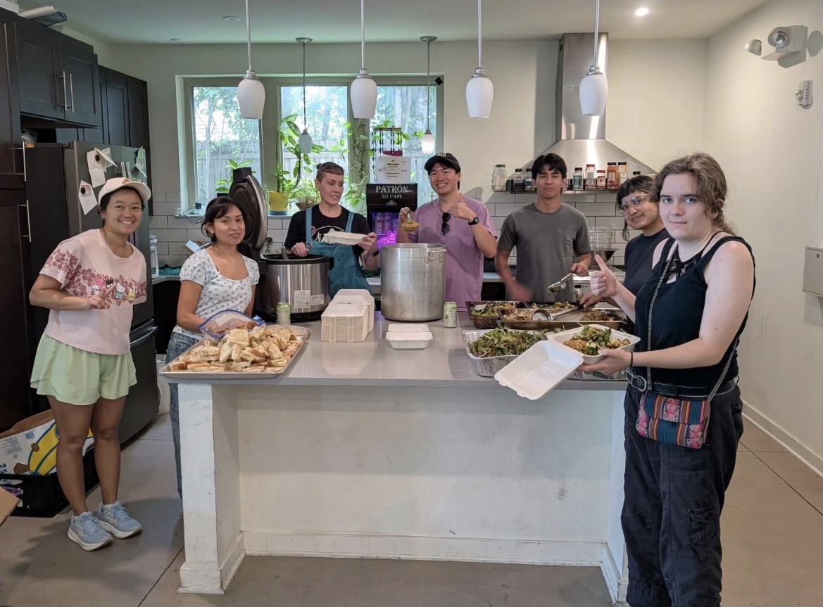Volunteers around a kitchen island with pots, trays of food, and stacks of takeout containers